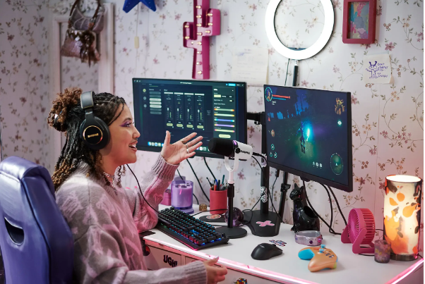 デスク上にデュアルモニターやキーボードを配置し、ヘッドホンを着けた人物がマイクに向かって話しながら配信やゲームを行うセットアップ