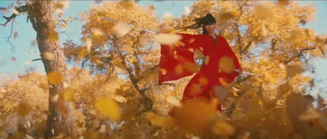 A woman in flowing red garments holding a sword out to her side through falling yellow leaves.