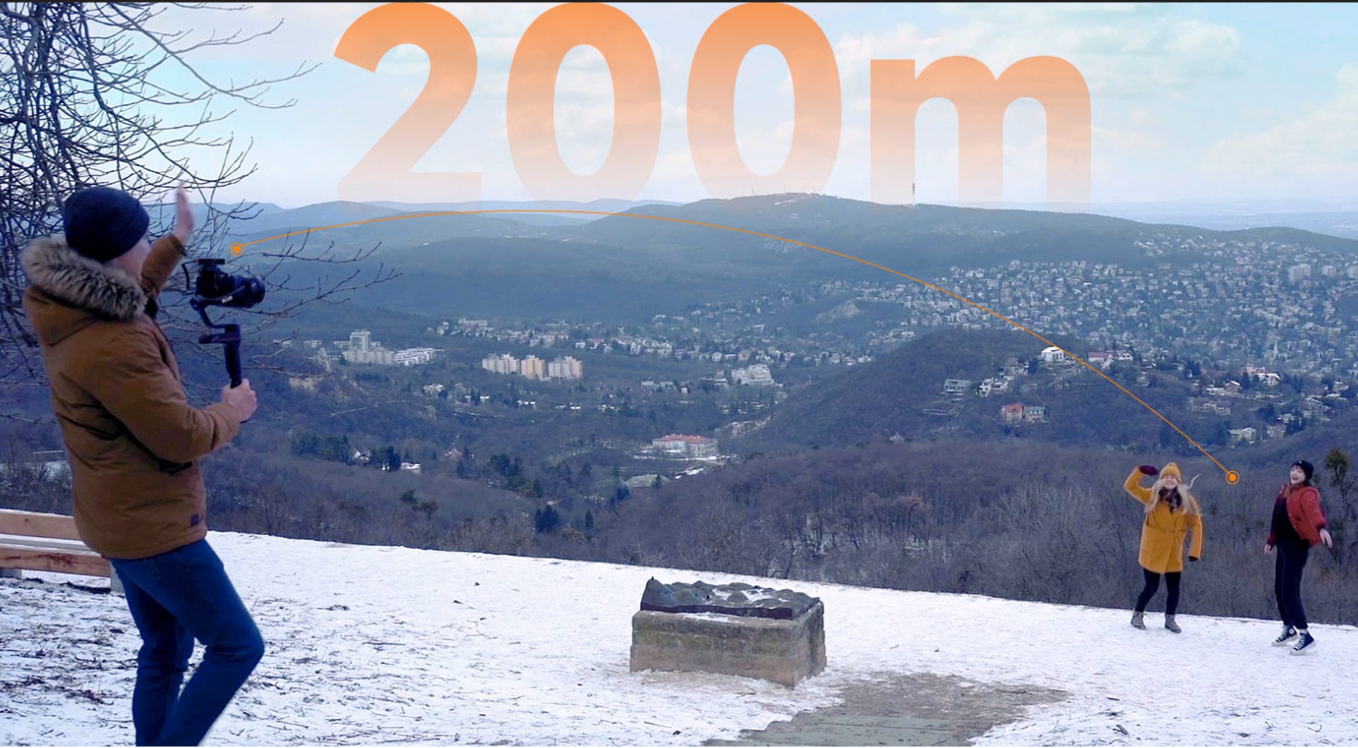 雪の積もった丘の上で、カメラを構える男性と遠くに離れた2人の女性。カメラから女性たちへオレンジ色の線が伸び、上空に「200m」の大きな文字が表示される。
